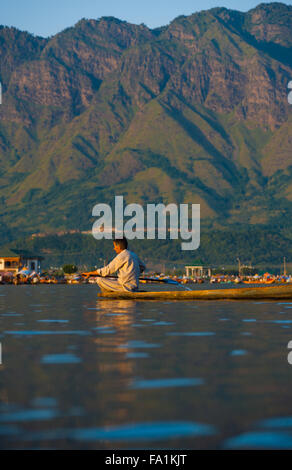 Kashmiri Muslim man rows his boat on the tourist destination of Dal Lake, surrounded by mountains in Kashmir Stock Photo