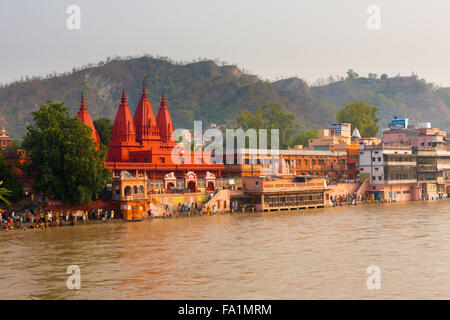 Hindus gathering at a pilgrimage spot near a red temple for bathing and cleansing in the Ganges River for purification Stock Photo