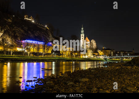 The outside of the Pfarrkirche Mülln (Roman Catholic Parish) Church in Salzburg at night from the River bank. Other buildings ca Stock Photo