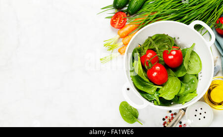 fresh organic garden vegetables in colander bowl on white rustic stone background, healthy cooking concept Stock Photo