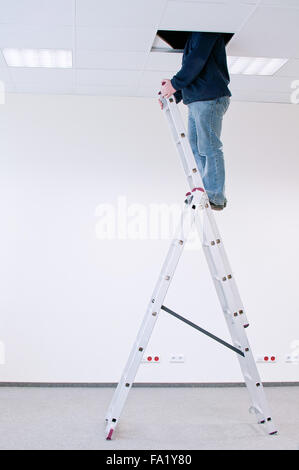 worker on a ladder, peering through a hole in the ceiling Stock Photo