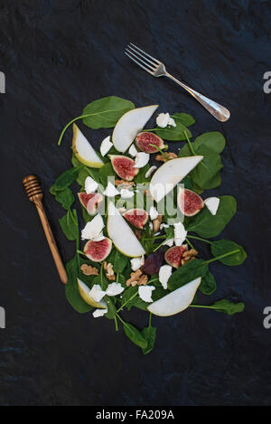 Salad with pears, baby spinach, figs, walnuts, goat cheese and honey on black stone background, top view Stock Photo