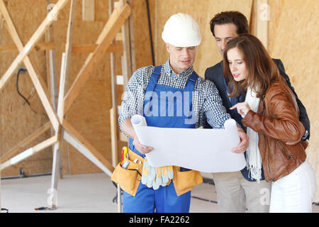 Foreman shows house design plans to a young couple Stock Photo