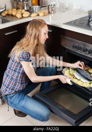 Long-haired woman cooking raw fish in oven at home kitchen Stock Photo