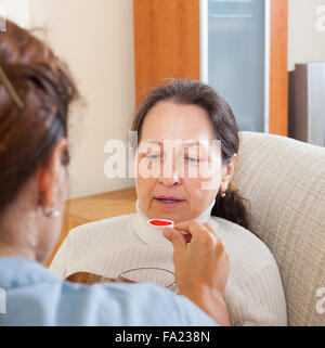 Girl giving the cough syrup to mature woman at home Stock Photo