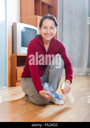 mature woman polishing parquet  with  polish at home Stock Photo