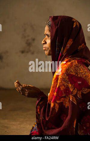 Side profile of Indian woman in red sari, shawl begging with her cupped hands out at the entrance of a mosque asking for money Stock Photo