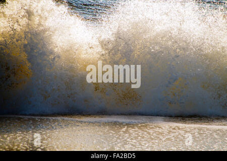 Close up of a big, colorful, ocean wave in a big tumble and splash with blue water behind it and sucking up water in front Stock Photo