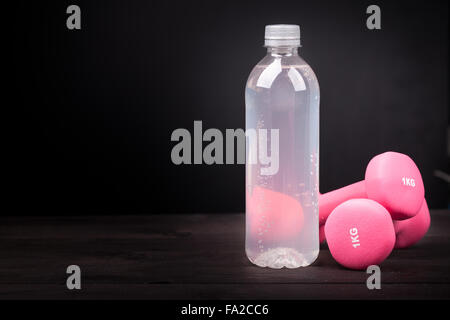 Sport equipment. Water bottle and pink dumbbell on a black wooden table and background with copy space Stock Photo