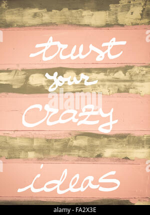 Concept image of Trust Your Crazy Ideas motivational quote hand written on vintage painted wooden wall Stock Photo