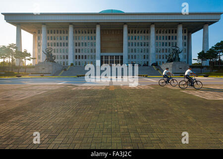 Policemen riding bicycles past the front of the National Assembly building, home to the legislative branch of government, in Seo Stock Photo