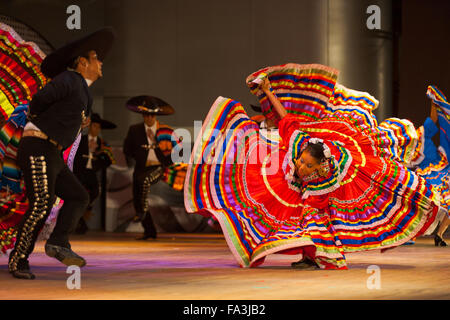 Female Mexican Jalisco dancer bent over in fluttering orange dress spinning, twirling at a folkloric dance outdoor free performa Stock Photo