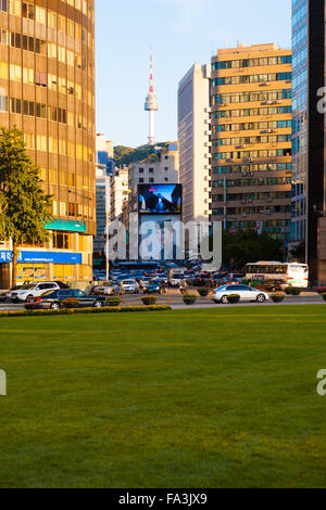 N Seoul Tower, a major tourist attraction, is visible between downtown office buildings from the grass plaza at city hall in Seo Stock Photo