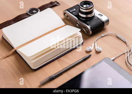 Opened blank notebook, old camera, tablet computer with earphones, watch and pen lying on wooden table Stock Photo