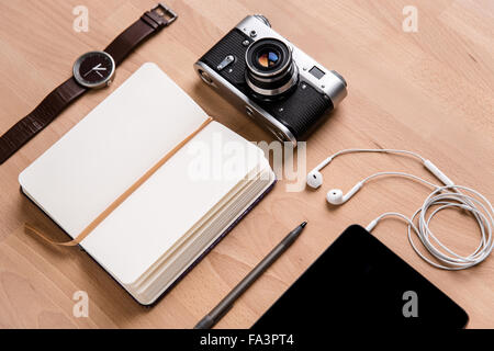 Opened notepad with white blank pages, tablet computer with earphones, old camera watch and pen on wooden table Stock Photo