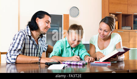 Teenager schoolboy and his parents together doing homework in home Stock Photo