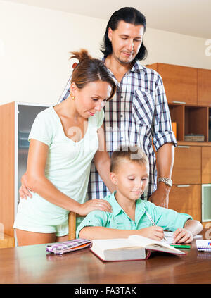 teenager schoolboy doing homework against cheerful parents in home interior Stock Photo