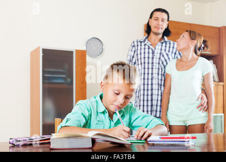 teenager schoolboy doing homework  against parents in home interior Stock Photo