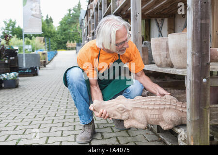 Male gardener putting crocodile sculpture on shelf in garden centre, Augsburg, Bavaria, Germany Stock Photo