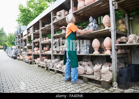 Male gardener arranging ceramic sculpture in shelf, Augsburg, Bavaria, Germany Stock Photo