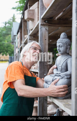Male gardener examining Buddha sculpture in greenhouse, Augsburg, Bavaria, Germany Stock Photo