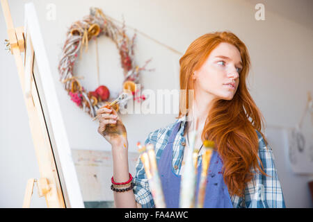 Cute lovely young woman painter with long red hair working in art workshop Stock Photo