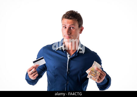 Young man holding banknotes and credit card, choosing between the two means of payment. Isolated, studio shot Stock Photo