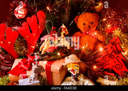 some gifts and some retro toys, such as a teddy bear, a horse or a marionette, under a christmas tree ornamented with lights, ba Stock Photo