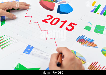 closeup of a young caucasian businessman at his office desk full of graphs and charts observing a chart with a downward trend du Stock Photo