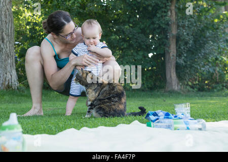 Baby boy and his mother looking at cat in lawn, Munich, Bavaria, Germany Stock Photo