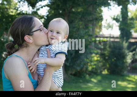 Mother kissing her baby boy in lawn, Munich, Bavaria, Germany