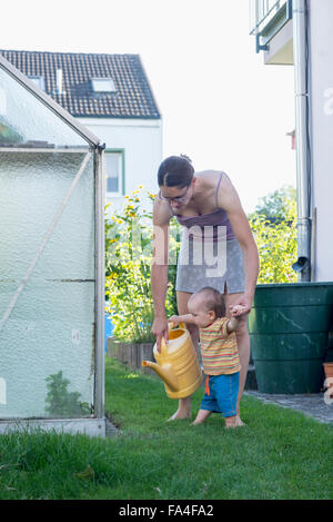 Mother and baby son holding a watering can in a lawn, Munich, Bavaria, Germany Stock Photo