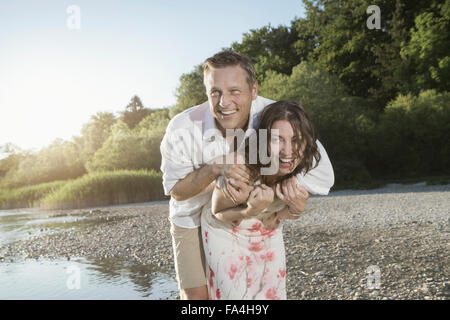 Mature woman giving piggyback ride to her husband at lakeside, Bavaria, Germany Stock Photo