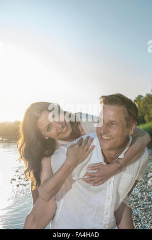 Mature man giving piggyback ride to his wife at lakeside, Bavaria, Germany Stock Photo
