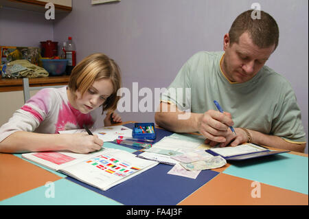 Young girl doing her homework while her father writes a cheque to pay a bill in the kitchen, Stock Photo