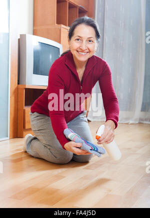 mature housewife polishing parquet floor with furniture polish Stock Photo