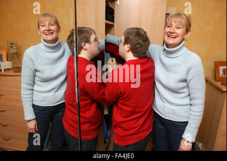 Boy putting clothes away in his wardrobe while his mother watches him, Stock Photo