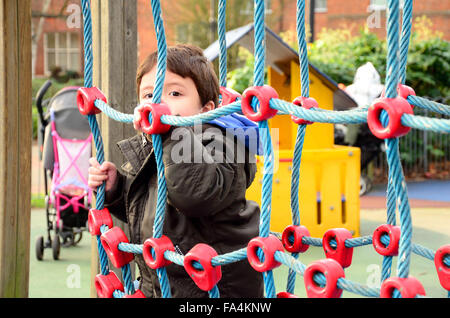A young boy playing on a net which is part of a climbing frame in a children's playground. Stock Photo