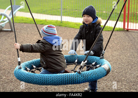 Two young boys play on a swing in a playground in Windsor Stock Photo
