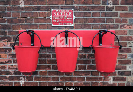 three red fire buckets hanging on a brick wall Stock Photo