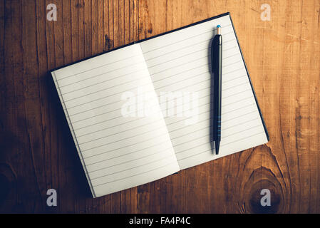 Top view of open notebook with blank pages and pencil on old wooden desk, retro toned image as copy space Stock Photo