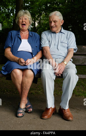 Older couple sharing a joke whilst sitting on a bench in the park , Stock Photo