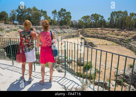 Women travel, rear view of two female friends visiting the ruins of the roman amphitheatre in the Archaeological Park in Syracuse, Sicily, Stock Photo