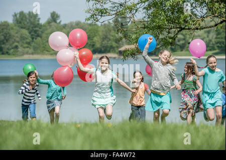 Children running in park with balloons, Munich, Bavaria, Germany Stock Photo
