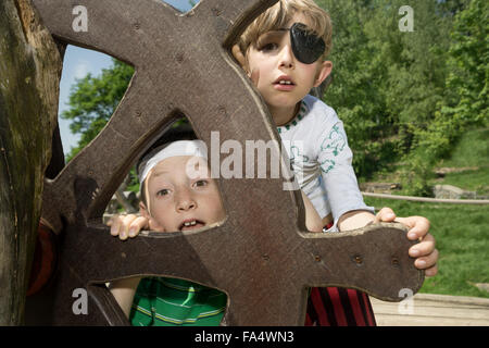 Two boys peeking from rudder of a pirate ship in adventure playground, Bavaria, Germany Stock Photo