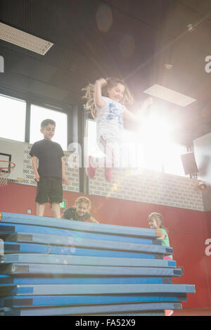 Children jumping from stack of sport mats in sports hall, Munich, Bavaria, Germany Stock Photo