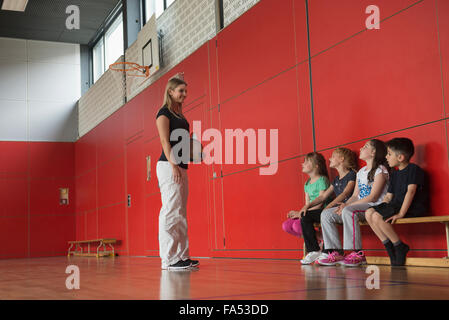 Teacher giving advice for group game to children in sports hall, Munich, Germany, Bavaria Stock Photo