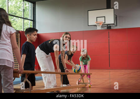 Teacher and students carrying bench in sports hall, Munich, Bavaria, Germany Stock Photo