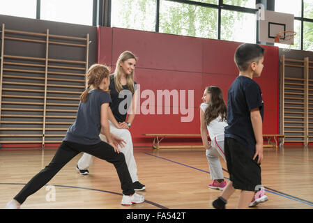 Teacher doing extension exercise with school children in sports hall, Munich, Bavaria, Germany Stock Photo