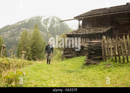 Mature hiker passing by cottage at rainy day, Austrian alps, Carinthia, Austria Stock Photo